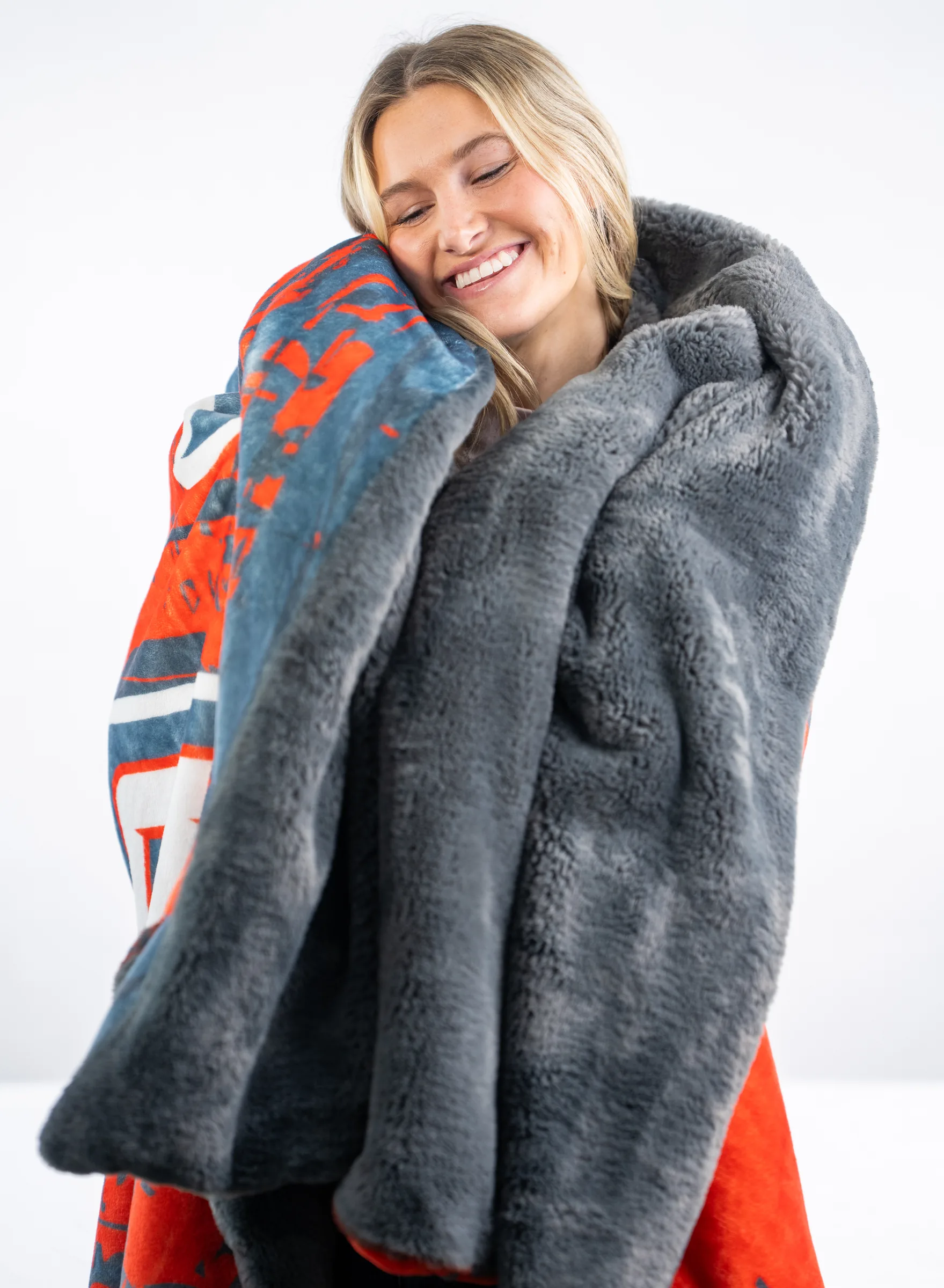 A woman resting her cheek into the deep grey faux-fur back of a Swanky blanket, the printed face visible at the fold